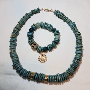 Dark Turquoise graduated disc bead necklace with Gold plated lobster clasp closure. The matching stretch bracelet features a gold-plated antique coin charm.